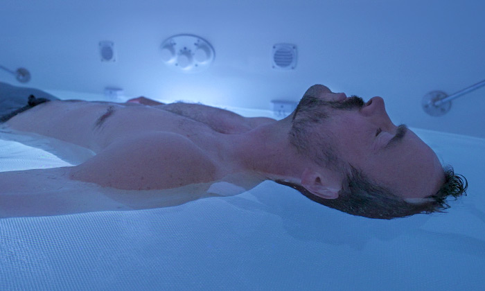 A man floating in a floatation tank - fully relaxed, and recovering himself.